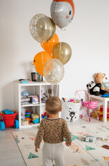 A boy walks into a room decorated with orange birthday balloons