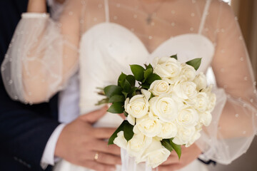 The groom hugs the bride with a bouquet in his hands