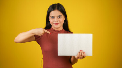 Beautiful young woman holding and pointing finger at empty blank white board, your text here concept, Asian Indian girl isolated over colour background studio