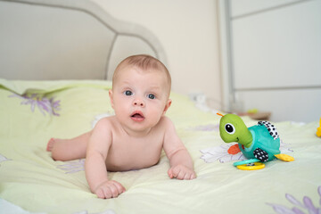 Baby lies on the bed with a toy