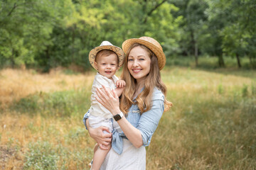 mother holds her son in her arms in a meadow in summer in straw hats