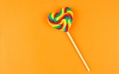 Rainbow colored heart shaped lollipop on orange background