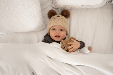 Cute baby lies in a cap in a crib with a teddy bear