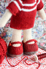 Cute knitted teddy bear toy - amigurumi handcraft with knitting tools and wool (focus on shoes to show handcraft details.)