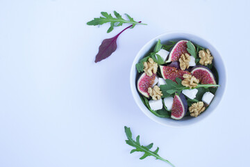 Salad with arugula, feta cheese, figs and walnuts in the white bowl on the white background. Top view. Copy space.