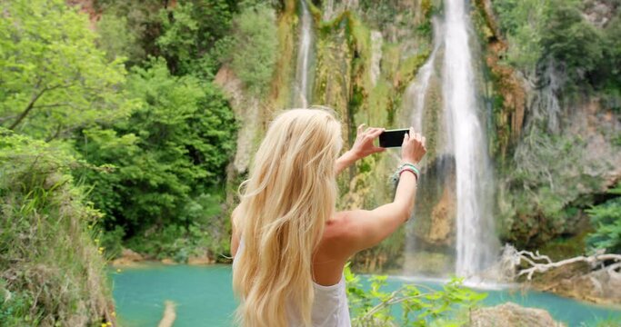 Phone, nature and woman taking a picture of waterfall on a summer vacation or adventure. Travel, water and girl with freedom taking photo of fountain, river or lake with mobile on holiday or journey.