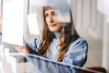 Creative young businesswoman sticking a document to a glass wall