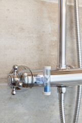 A shower tap with an hourglass attached to save energy and water