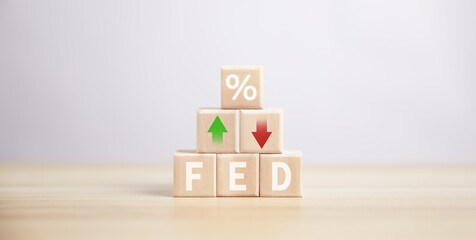 wooden cube blocks lined up With the fed percentage symbol and interest rate up and down arrows.