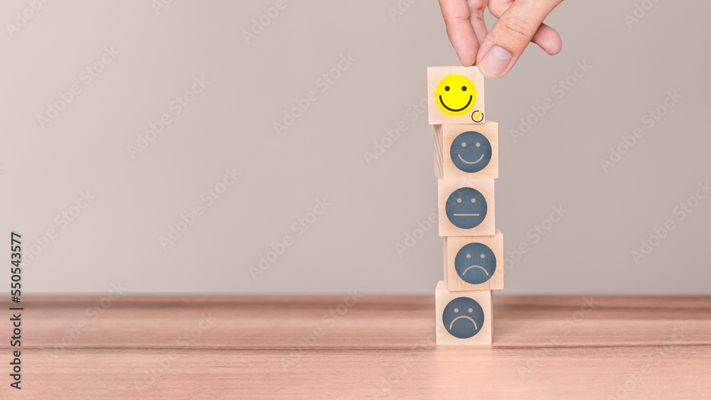 Poster hand putting a wooden cube block with a smile face icon on wood table. concept of customer services 