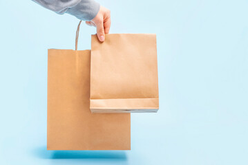 Female hand holds a brown cardboard bags on blue background, food delivery concept.