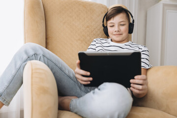 Teenage boy in wireless headphone using tablet having video chat on internet online at home. Child watching movie, playing video game. Social media concept. Online education. Distance learning © Lyubov