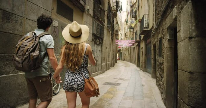 Couple, tourist and holding hands walking on city street for travel, vacation or adventure with backpack and wanderlust. Man and woman together in Barcelona for holiday, sightseeing and architecture