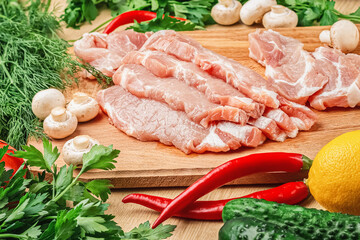 Fresh pork meat steaks on a wooden board. Mushrooms, tomatoes, lemon, parsley, dill and cucumbers. Ingredients for the recipe. Close-up.