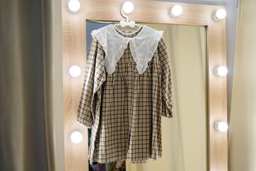 Beautiful beige checkered dress for girls. Dress with a white collar in a fitting room with a large mirror. Children's clothing store. Sale in a children's clothing store.