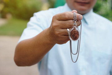 Closeup man in blue shirt holds Thai Buddha amulet necklace.  Concept, faith and belief of Buddhist for holy to protect from dangers, bring good luck, business prosperity and wealth.   