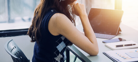 Young business woman sitting in office at table and using smartphone. On desk is laptop and tablet computer, on screen charts and graphs. Woman analyzing data. Student learning online.