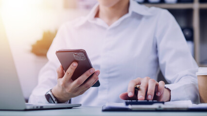 Young business woman sitting in office at table and using smartphone. On desk is laptop and tablet computer, on screen charts and graphs. Woman analyzing data. Student learning online.