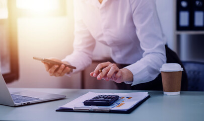 Young business woman sitting in office at table and using smartphone. On desk is laptop and tablet computer, on screen charts and graphs. Woman analyzing data. Student learning online.