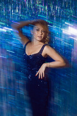 sexy woman blonde in a blue dress in sequins on a blue background blue sparkles holiday birthday, christmas, party. model poses in front of the camera.