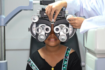 Smiling little girl testing vision or sight with optical phoropter in modern ophthalmology clinic