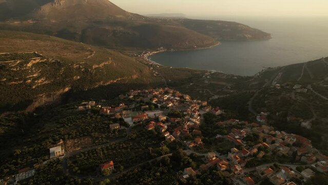 A high altitude drone flight above an old greek village at golden hour reveals the sea in the background during summertime.