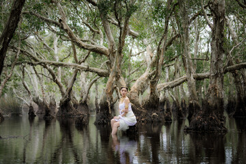 beautiful  Thai asian woman in white dress local tradition costume in the name is Nakee, sitting on tree stump in the lake in the botannical garden rayong thailand