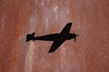 A hole in the shape of an airplane in rusting metal

