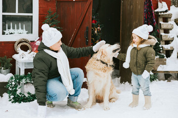 siblings girl sister and teenage cute boy brother in knitted sweater and hat having fun with first snow and cute pet dog labrador at porch of country house, concept of winter spirit and Christmas