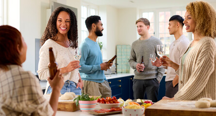 Group Of Friends At Home In Kitchen With Drinks Making Food For Party
