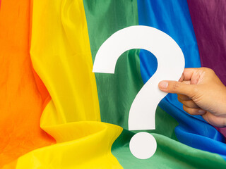Hand holding of a question mark over the rainbow flag or LGBT flag background