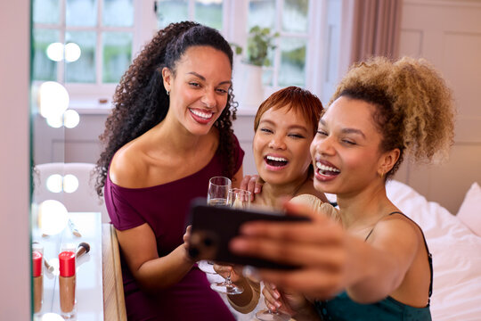 Group Of Female Friends At Home Dressed Up And Drinking Champagne Posing For Selfie Before Night Out