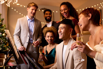 Group Of Friends Around Piano Celebrating At Christmas Or New Year Party Together
