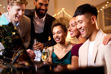 Group Of Friends Around Piano Celebrating At Christmas Or New Year Party Together