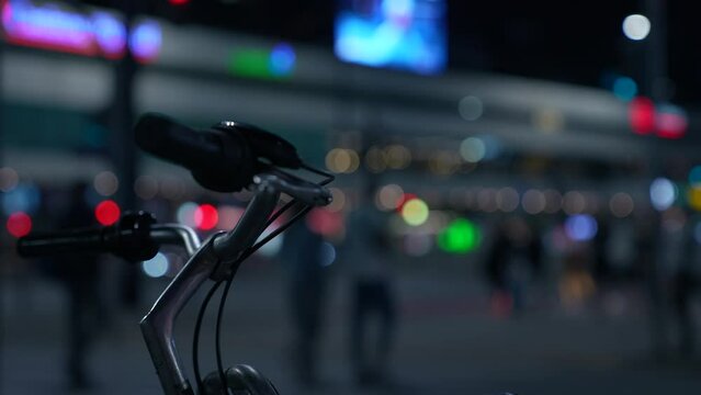 Bicycle and night city atmosphere. In the foreground in sharpness - the handlebars of a city bike. In the background - night city and the silhouettes of pedestrians crossing the road at the crosswalk