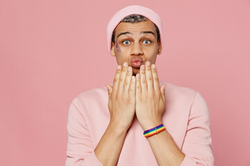 Young shocked surprised amazed astonished gay man wear sweatshirt hat hold hands near mouth cover isolated on plain pastel light pink color background studio portrait. Lifestyle lgbtq pride concept.