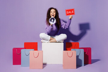 Full body young woman wear pullover sit near shopping paper package bag card sign with sale title text scream in megaphone isolated on plain pastel purple background Black Friday sale buy day concept.
