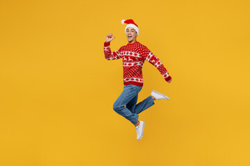 Fototapeta na wymiar Full body side view fun merry young man wear red knitted Christmas sweater Santa hat posing jump high run hurry up isolated on plain yellow background. Happy New Year 2023 celebration holiday concept.