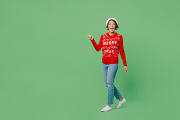 Full body side view merry young woman wear knitted xmas sweater Santa hat posing walk go point...