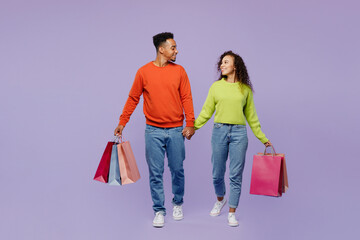 Full body front view young couple two friend family man woman in casual clothes together hold hand shopping package bags isolated on plain pastel purple background. Black Friday sale buy day concept