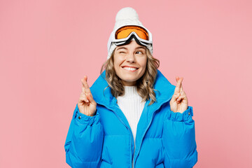 Snowboarder woman wear blue suit goggles mask hat ski padded jacket spend extreme weekend keep fingers crossed make wish isolated on plain pastel pink background Winter sport hobby trip relax concept.