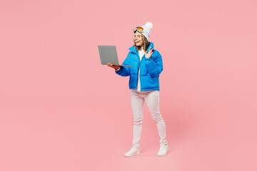 Snowboarder IT woman wear blue suit goggles mask hat ski jacket work hold use laptop pc computer waving hand isolated on plain pink background. Winter extreme sport hobby weekend trip relax concept. © ViDi Studio