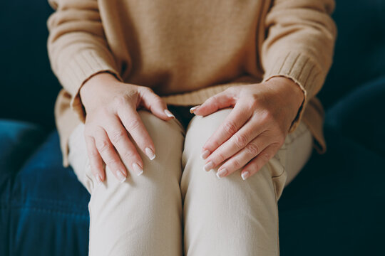 Cropped Close Up Photo Of Woman Wearing Beige Casual Clothes Sits On Dark Blue Sofa Couch Hold Hands With No Manicure On Knees Stay At Home Flat Rest Relax Spend Free Spare Time In Living Room Indoor.