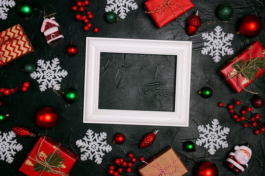 Blank white photo frame surrounded by Christmas decorations on a black background.