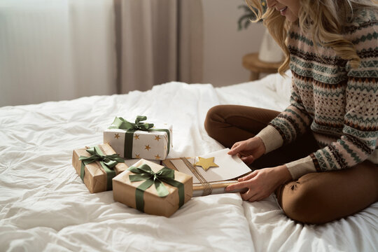 Caucasian woman sitting on bed and packing Christmas gift with greeting card
