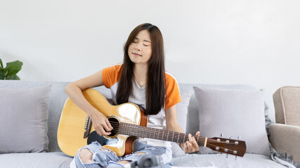 Asian female artist playing the guitar and singing happily in the living room, Relaxation with...