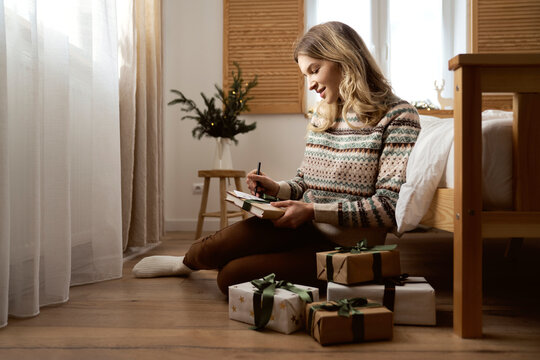 Caucasian woman sitting on floor and writing Christmas card