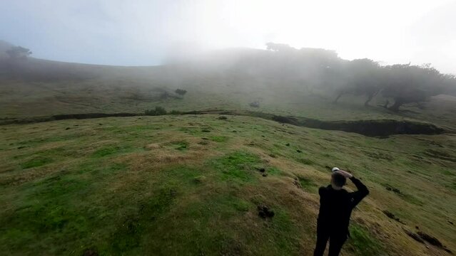 Aerial FPV footage of a man taking a picture in a foggy and cloudy day in Fanal forest, Madeira Island, Portugal