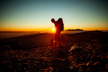 man walking in the middle of the mountain with montserrat in the background at sunset with red and orange colors of sunlight