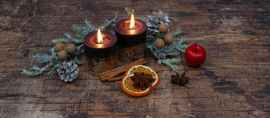 Zwei brennende Kerzen auf schäbigem Holz mit Zweigen einem Apfel Zimtsangen und Orangenscheiben,